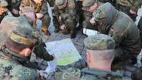 Mehrere Soldaten knien um eine Karte während einer darauf zeigt 