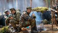 Personen in Uniform sitzen auf Baumstämmen im Wald und essen