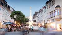 Bei Abenddämmerung sieht man den St. Johanner Markt mit barockem Marktbrunnen, drum herum befinden sich Touristen.