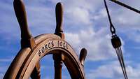 Ein Steuerrad aus Holz an Bord eines Segelschiffes.