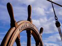Ein Steuerrad aus Holz an Bord eines Segelschiffes.