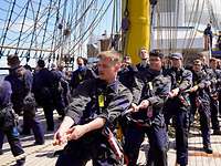 Junge Männer und Frauen ziehen auf einem Segelschiff gemeinsam an einem Seil.