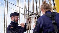 Ein Soldat in blauer Uniform malt auf einem Segelschiff Teile mit Farbe an.