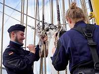 Ein Soldat in blauer Uniform malt auf einem Segelschiff Teile mit Farbe an.