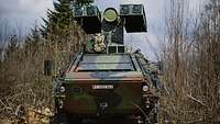 Auf einem Gelände steht ein Transportpanzer, auf dem eine Flugabwehrattrappe verbaut ist
