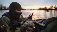 Ein bewaffneter Soldat in einem auf einem Fluss fahrenden Sturmboot bei Sonnenuntergang 
