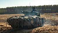 Durch die Sonne beschienen steht ein Schützenpanzer Leopard auf offenem Gelände, dahinter ist eine Baumkette erkennbar.