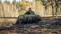 Ein Schützenpanzer Puma fährt mit hoher Geschwindigkeit über offenes Gelände, im Hintergrund sind Baumketten erkennbar.