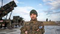 Ein Soldat steht in die Kamera blickend vor militärischen Fahrzeugen mit Raketenstartvorrichtungen