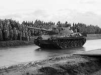 Ein Kampfpanzer Leopard 1 fährt an zusehenden Soldaten auf einer Asphaltierten Straße vorbei.