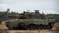 Auf offenem Gelände steht ein Leopard-2A4-Kampfpanzer, im Hintergrund ist ein Helikopter zu erkennen.