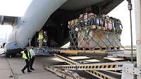 Drei Männer mit gelben Warnwesten laden mit einer speziellen Hebemaschine ein graues Flugzeug ab.