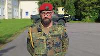 Ein Soldat mit rotem Barett, Brille und Bart schaut freundlich in die Kamera.