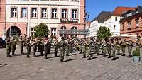 Auf einem sonnigen Marktplatz steht ein Militärorchester und spielt.
