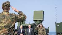 Olaf Scholz und Boris Pistorius stehen vor Militärfahrzeugen, zwei Soldaten salutieren.