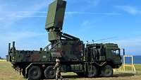 Ein Soldat steht vor einem großen Militärfahrzeug.