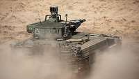 Eine gepanzertes Fahrzeug mit einem großen Geschütz fährt auf sandigem Untergrund.