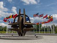 Die NATO-Sternenskulptur und dahinter wehen die Flaggen der Mitgliedsstaaten an Flaggenmasten