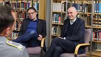 Zwei Männer sitzen bei einem Interview nebeneinander in einer Bibliothek
