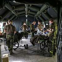 Mehrere Personen in Uniform behandeln verletzte Personen in einem großen Tunnelzelt.