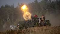 Auf einer Waldlichtung wird von einer grün getarnten Trägerplattform ein Panzermörser abgefeuert.