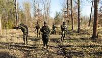 Fünf Soldaten laufen mit Abstand durch den Wald und sichern mit ihren Waffen in alle Richtungen. 
