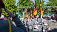 Soldaten in Uniform und mit Fahnen marschieren auf einem Appellplatz