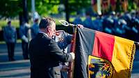 Ein Mann im Anzug befestigt ein Band an einer Deutschlandfahne