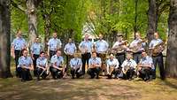Musiker stehen mit Instrumenten in einer grünen Allee