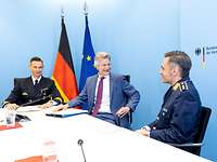 Ein Soldat spricht mit einem Soldaten und einem Mann an einem Tisch sitzend