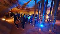 Menschen stehen in einer bunt beleuchteten Höhle und tragen Schutzhelme.
