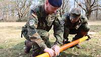 Geophysikalischen Sonde Zwei Soldaten knien auf einer Wiese und verschrauben zwei Rohe miteinander.
