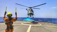 Hubschrauber bei der Landung Ein Hubschrauber wird durch eine Person zur Landung auf einem Schiff eingewiesen.
