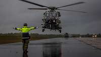 Ein Mann mit Warnjacke auf dem Rollfeld weist einen landenden Hubschrauber ein.