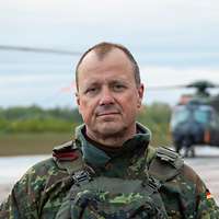 Auf einem grauen Flugfeld steht ein Soldat vor vielen hintereinander parkenden Hubschraubern.