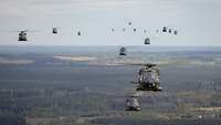 Zahlreiche verschiedene Hubschrauber fliegen in Formation, unter ihnen Landschaft.