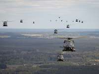 Zahlreiche verschiedene Hubschrauber fliegen in Formation, unter ihnen Landschaft.