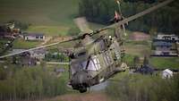 Ein Hubschrauber fliegt mit hoher Geschwindigkeit über einer Ortschaft.