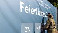 Eine Soldatin befestigt ein großes Plakat an einem Zaun.