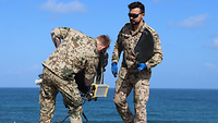 Zwei Soldaten bauen eine Antenne ab. Im Hintergrund sieht man das Meer.