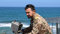 Ein Soldat überprüft eine Antenne, im Hintergrund das Meer