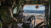 Ein Soldat schießt mit einem Maschinengewehr von einem Hubschrauber aus.