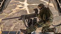 Ein Soldat steht auf der Rampe eines fliegenden Hubschraubers und schießt an einem Maschinengewehr.