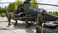 Vier Soldaten arbeiten auf einer Betonfläche an einem stehenden Kampfhubschrauber.