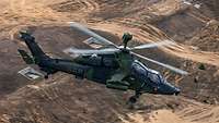 Luftaufnahme: Ein grüner Hubschrauber fliegt über eine weite braune Sandebene.