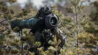 Ein Infanterist steht in einem kleinen Wald und hat eine Panzerabwehrrakete auf der Schulter. 