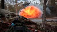Ein Soldat liegt an einem Hang und beobachtet eine Explosion. Ein Feuerball steigt auf.