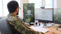 Rückenansicht eines uniformierten Soldaten, der an mehreren Computerbildschirmen sitzt.