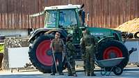 Soldatinnen und Soldaten im Gespräch mit einem Bauern vor einem Traktor