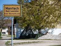 Ortseingangsschild mit einem Posten mit Tarnnetz im Hintergrund